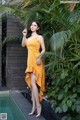 A woman in a yellow dress standing next to a pool.