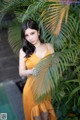 A woman in a yellow dress standing next to a palm tree.