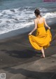 A woman in a yellow dress walking on the beach.