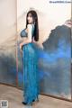 A woman in a blue dress standing in front of a painting.