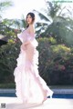 A woman in a pink dress standing next to a pool.