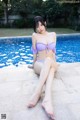 A woman in a purple bikini sitting by a swimming pool.