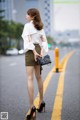 A woman in a white blouse and a green skirt is standing on the street.