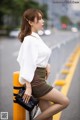 A woman in a white shirt and brown skirt leaning against a yellow pole.