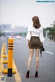 A woman walking down the street in a white blouse and brown skirt.