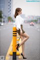 A woman leaning against a yellow pole on the side of the road.