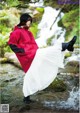 A woman in a red raincoat and white skirt standing in a stream.