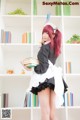 A woman in a maid outfit holding a stack of books.