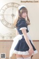 A woman in a maid outfit posing in front of a clock.