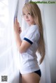 A woman in a white shirt and blue panties leaning against a curtain.