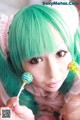 A girl with green hair holding two lollipops in her hands.