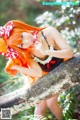 A woman with long orange hair sitting on a tree branch.