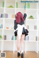 A woman in a maid outfit standing in front of a bookshelf.