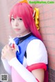 A woman with pink hair leaning against a brick wall.