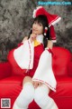 A woman in a red and white outfit sitting on a red couch.