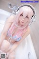 A woman with pink hair sitting in a bathtub with headphones on.