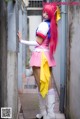 A woman in a pink dress and white boots leaning against a wall.