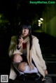 A woman in a white coat and scarf sitting on the ground.