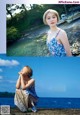 A woman in a blue dress sitting on a rock by the water.