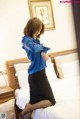 A woman in a blue shirt and black skirt standing on a bed.