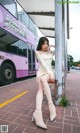 A woman sitting on a bus stop next to a bus.