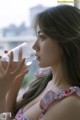 A woman drinking water from a glass by a window.