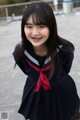 A woman in a school uniform smiles at the camera.