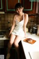 A woman sitting on a kitchen counter with a cake on a cutting board.