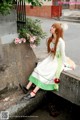 A woman in a white and green dress sitting on a stone wall.