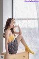 A woman sitting on top of a wooden dresser next to a window.