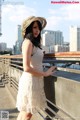 A woman in a white dress and hat posing for a picture.