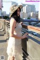 A woman in a white dress and hat standing on a bridge.