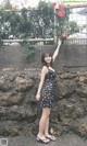 A woman standing in front of a stone wall holding a flower.