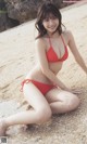 A woman in a red bikini sitting on a beach.