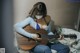 A woman sitting on a bed playing a guitar.