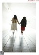 Two young girls holding hands while walking down a hallway.