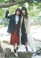 Two young women standing next to each other in front of a tree.