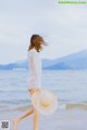 A woman walking on the beach with a hat on.