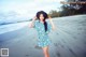 A woman in a blue and white dress and hat on a beach.