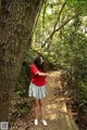 A woman in a red shirt and gray skirt standing next to a tree.