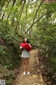 A woman standing in the middle of a forest holding a red scarf.