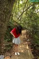 A woman in a red shirt and gray skirt standing on a path in the woods.