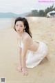 A woman in a white dress crouching on the beach.