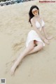 A woman in a white bikini sitting on the beach.