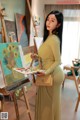 A woman in a yellow dress is painting on an easel.