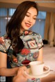 A woman in a cheongsam holding a cup of coffee.