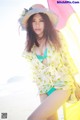 A woman in a bikini and hat posing on the beach.