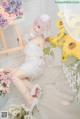 A woman in a white dress sitting on a white rug next to flowers.