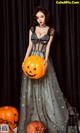 A woman in a black dress holding a pumpkin.