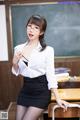 A woman in a white shirt and black skirt posing in front of a blackboard.